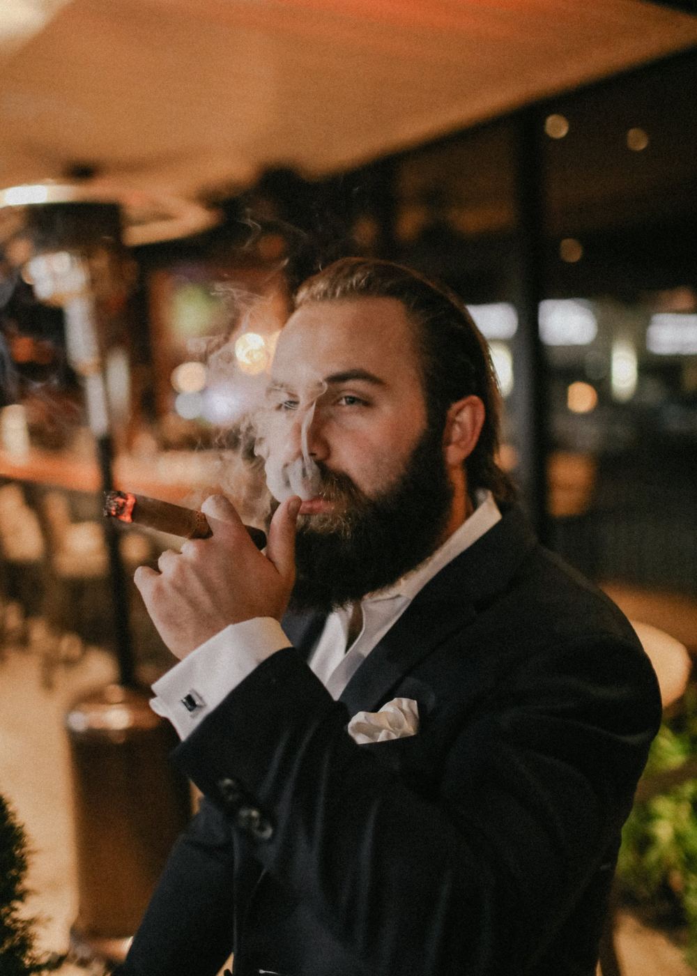 A man in a dark suit smoking a cigar at night